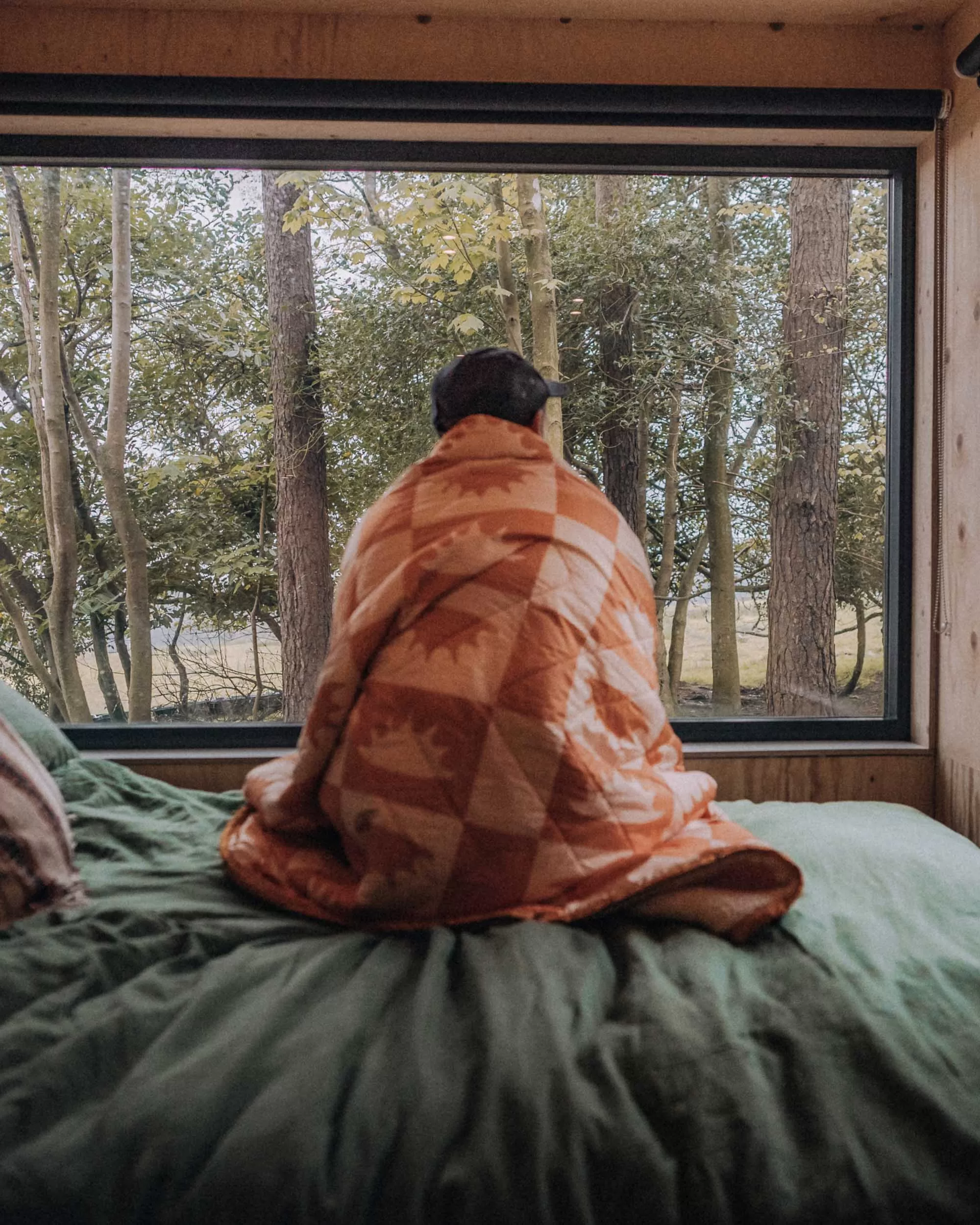 A man with a blanket wrapped around him looking out of a window