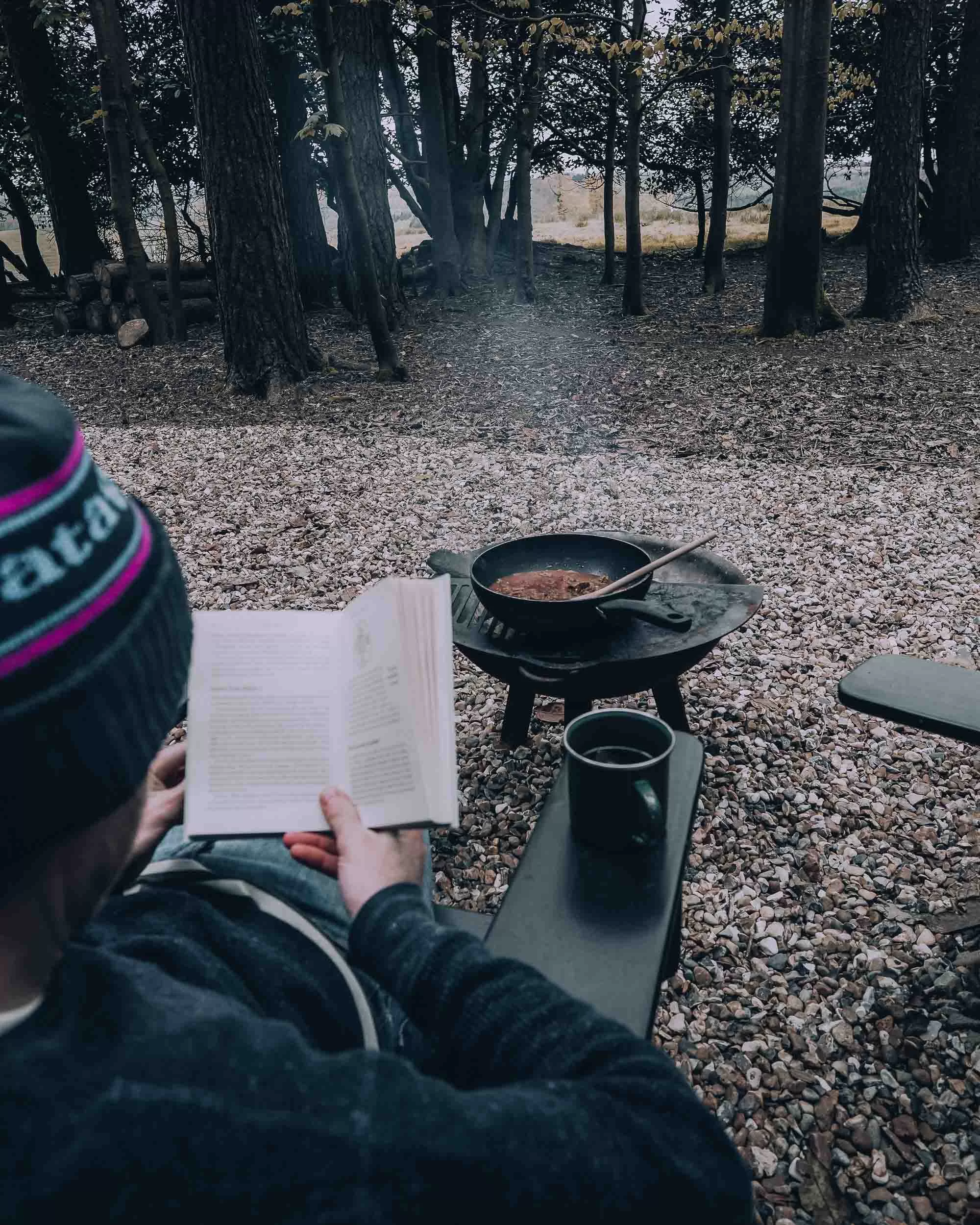 Man reading a book and cooking outdoors