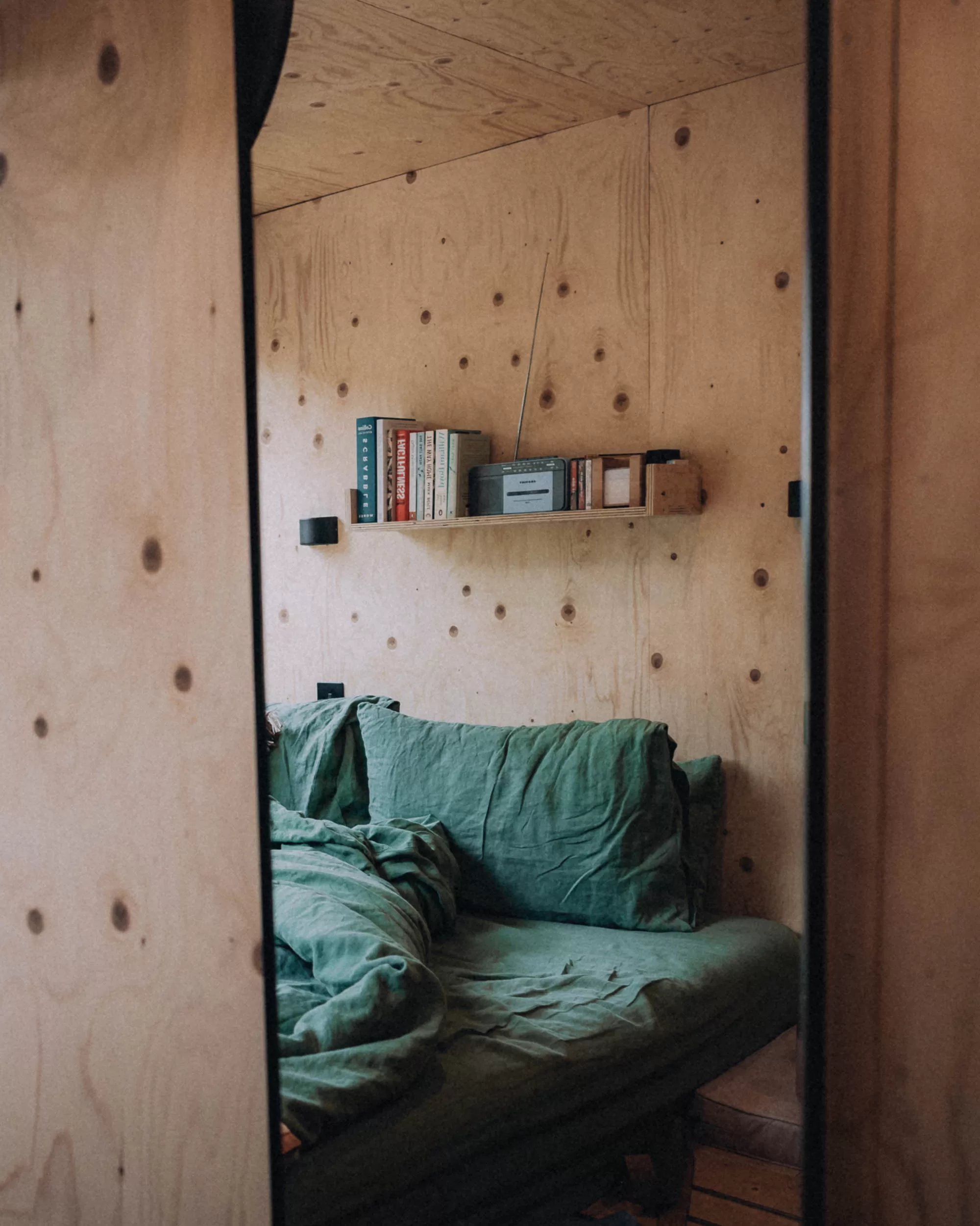 A bed and shelf seen in the reflection of a mirror