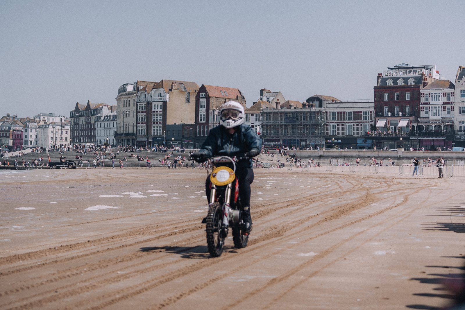 Man on motorcycle rides along a sandy beach.