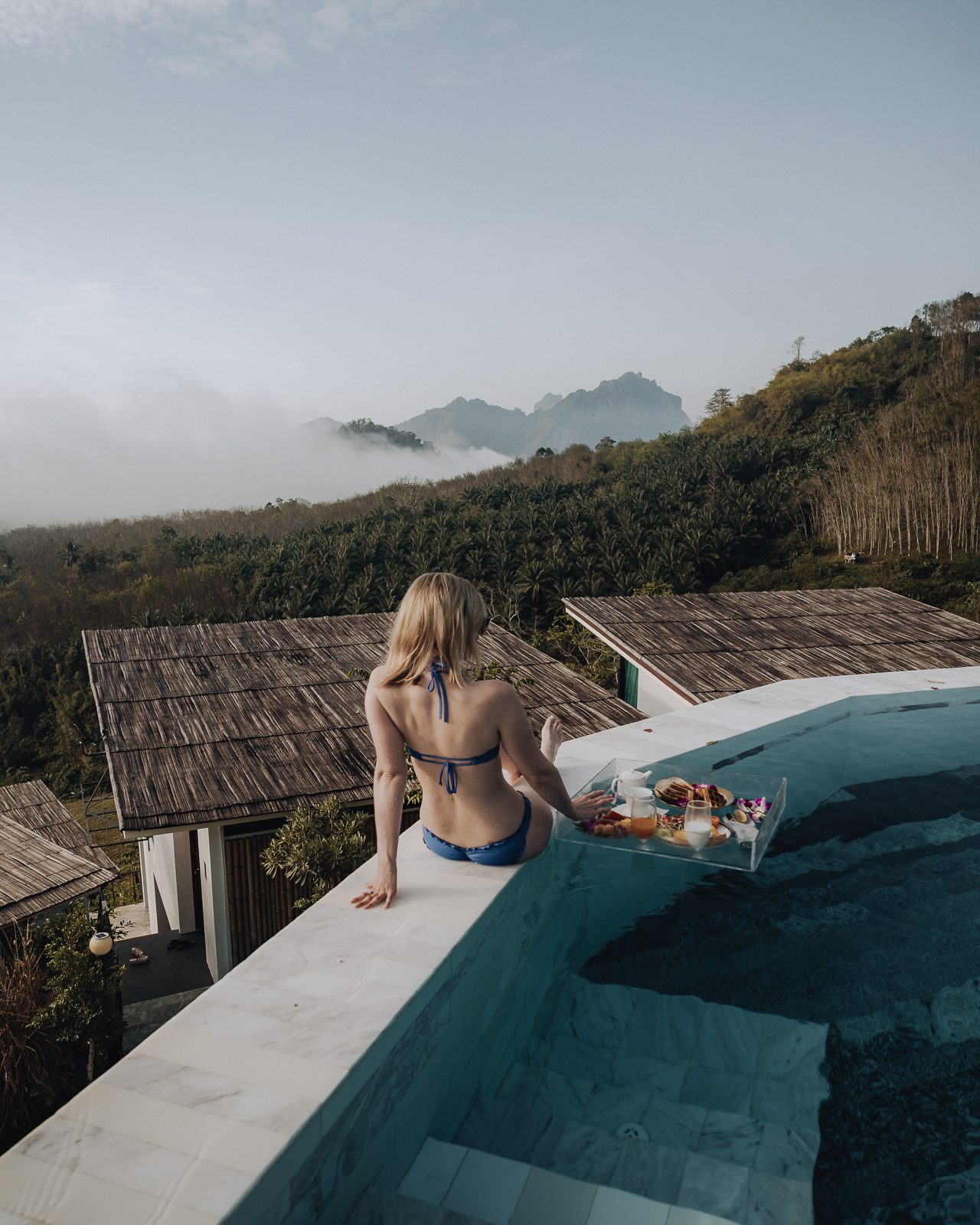 Woman wearing a bikini sitting beside pool.