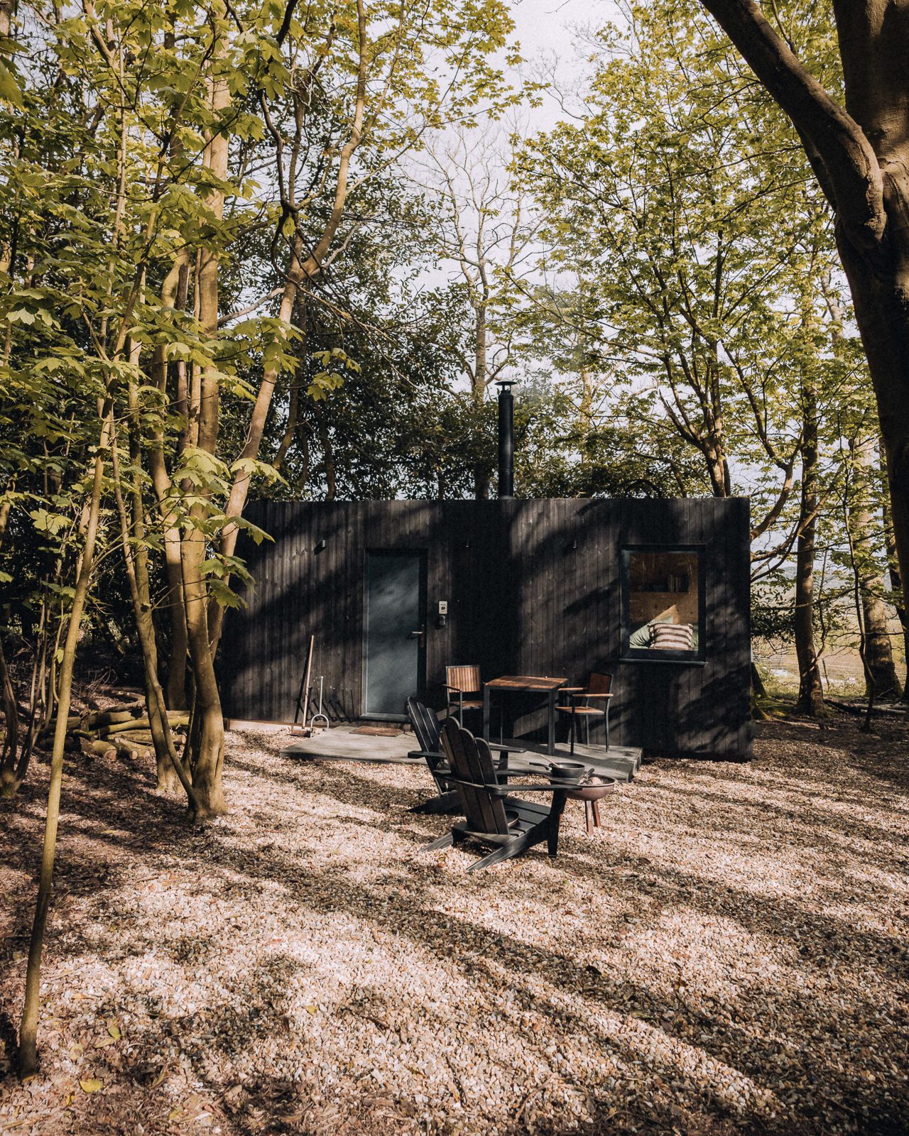 A woodland cabin clad in dark wood is surrounded by trees.