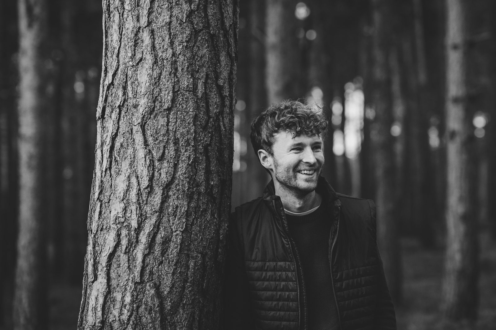 Man smiling while leaning against a tree.