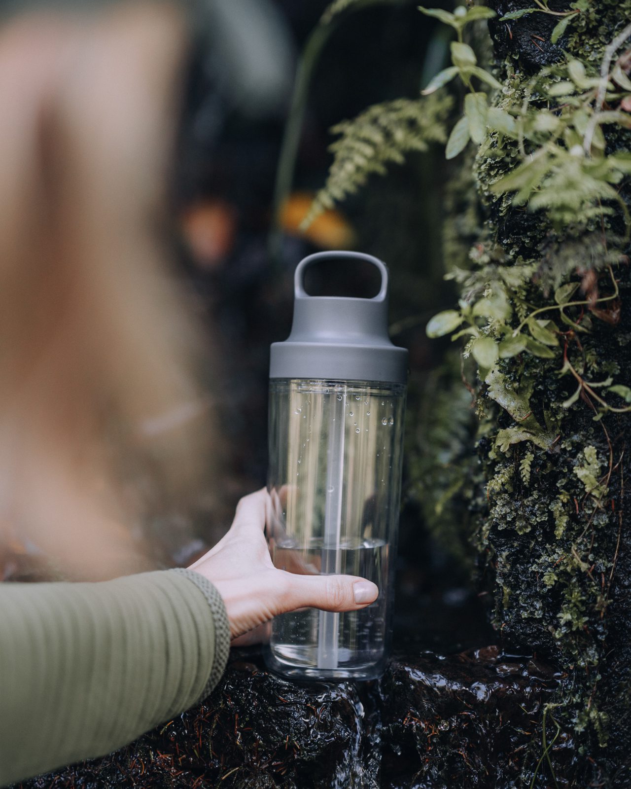 Woman holds clear water bottle against an outdoor spring.