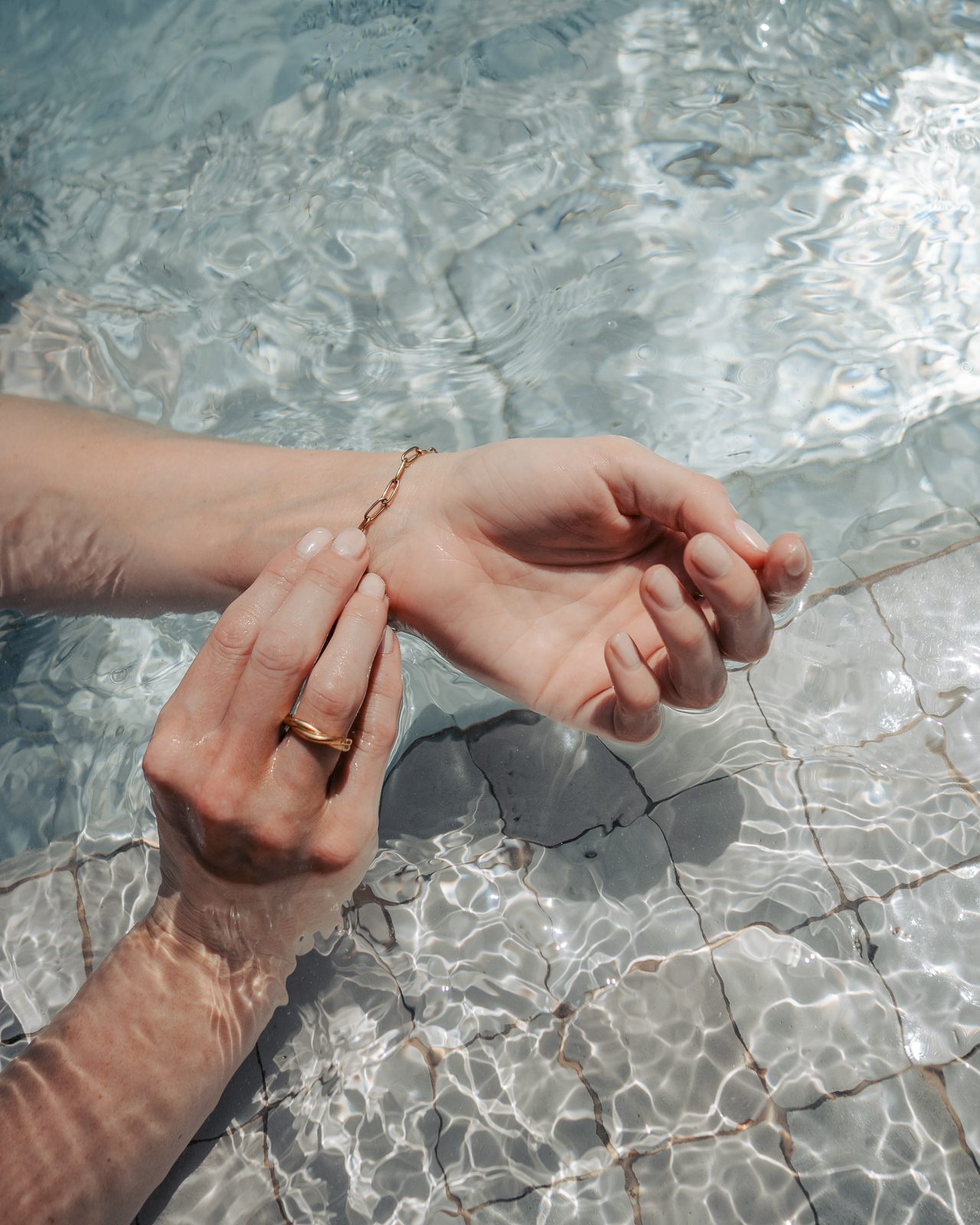 Woman adjusting gold chained bracelet in pool.