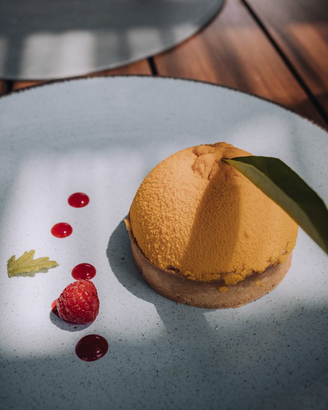A lemon tart with raspberry decorations on a clean plate.