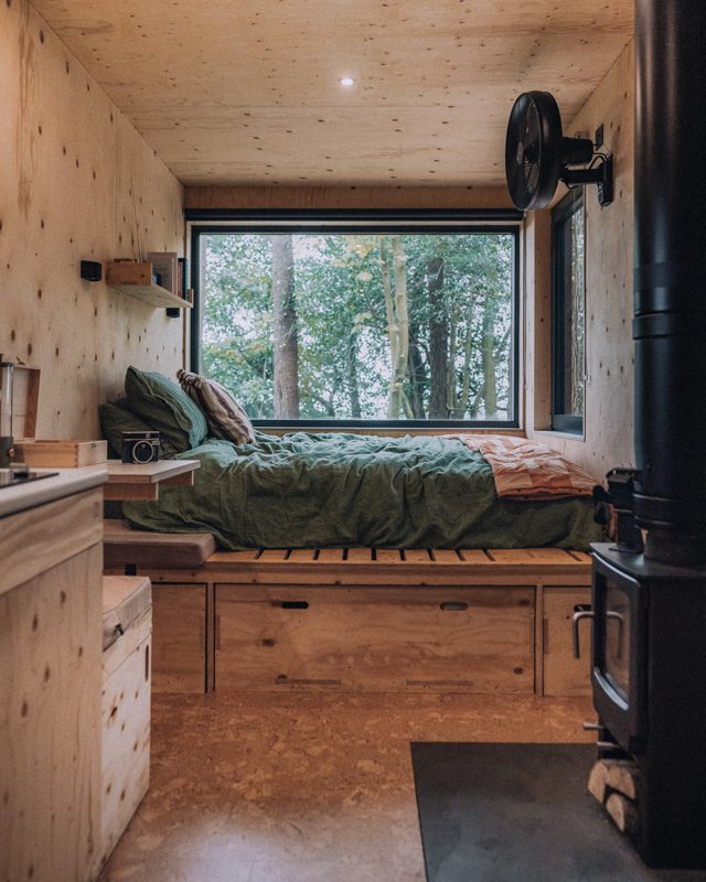 Interior of basic cabin setup with bed and log burner.