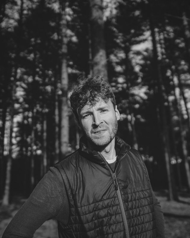 Black and white portrait of a man posing in the woods.