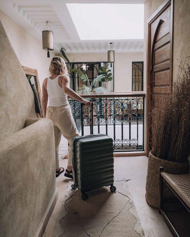 Woman stands with her wheeled luggage in corridor of hotel in Marrakech.