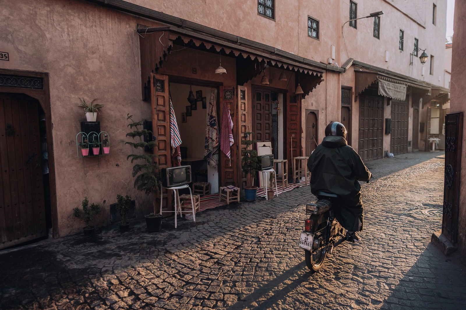 Man riding a motorbike through a Marrakech back street in warm morning light