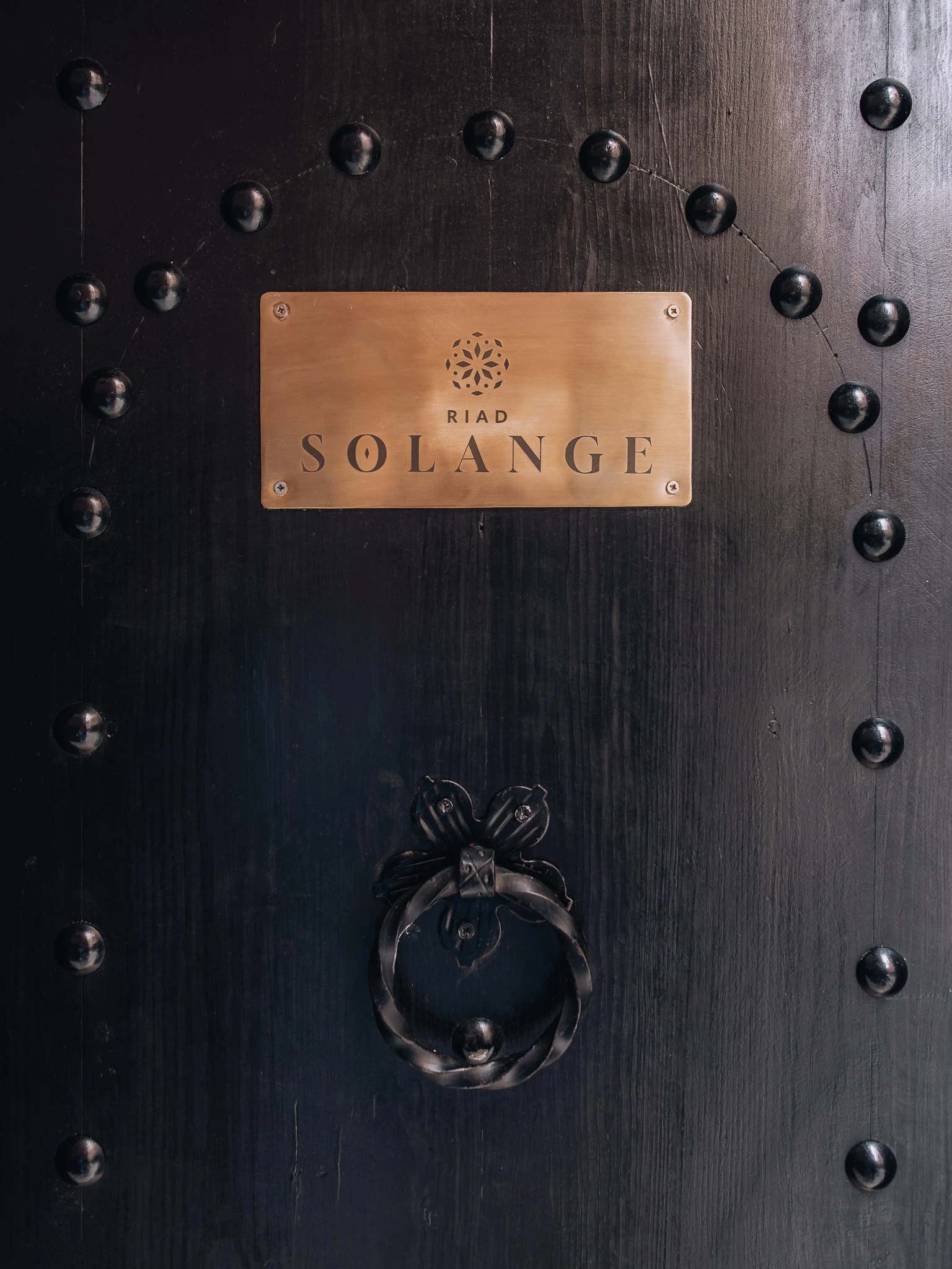 Traditional black entrance door with the Riad Solange gold sign in Marrakech